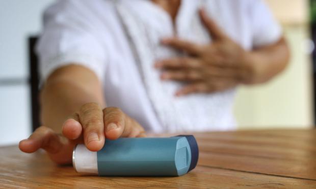 A person reaching for an inhaler close to the camera. In the background, they have one blurry hand over their chest.